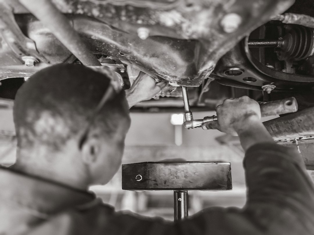 Mechanic working on car underside with wrench.
